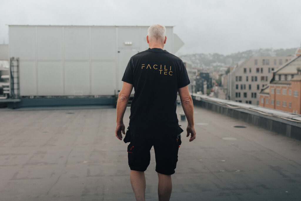 En man står med ryggen mot kameran på ett tak mitt i staden med lägenhetshus i bakgrunden en grå dag. Foto