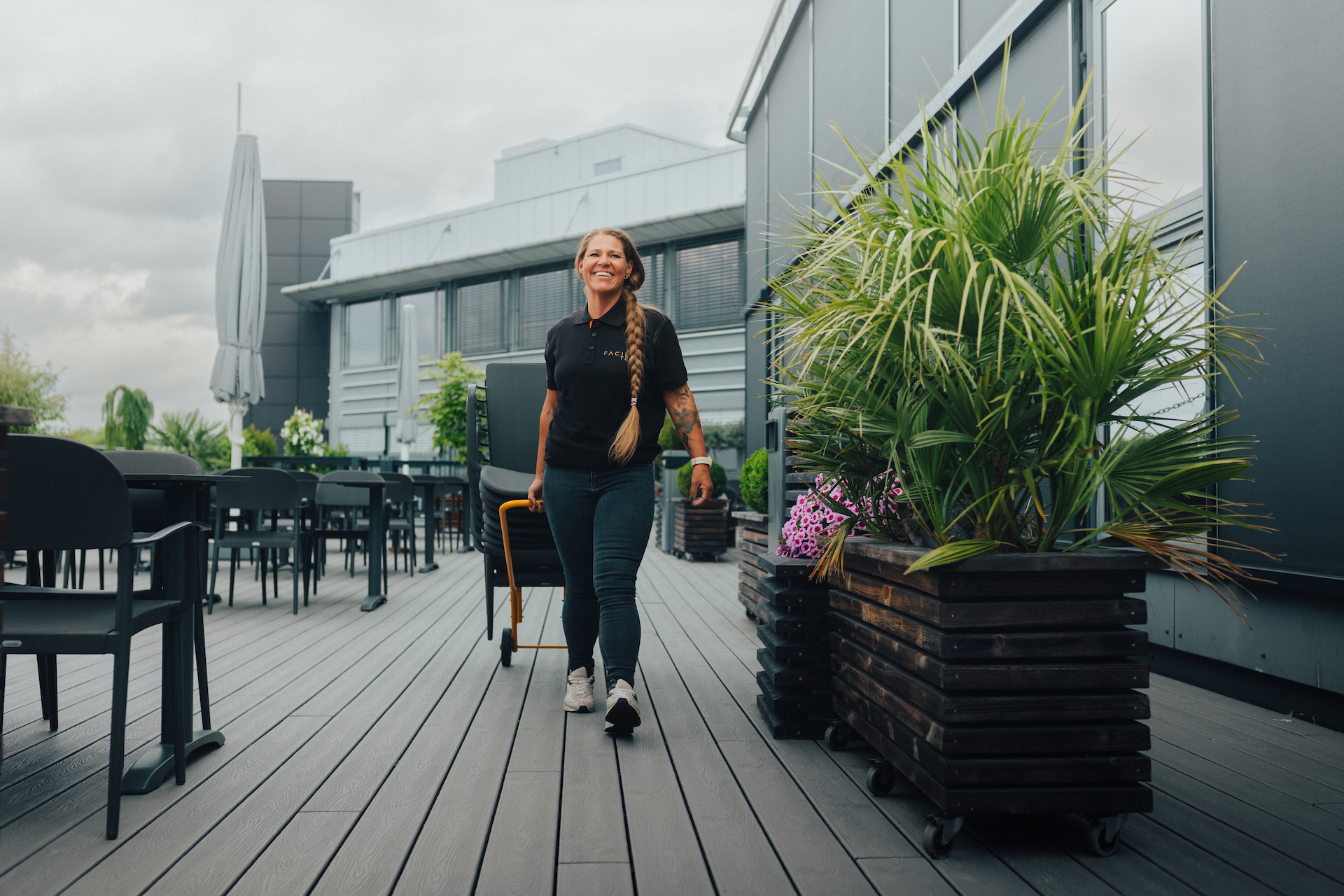 A smiling lady on a rooftop terrace is pulling a load of chairs. Photo.